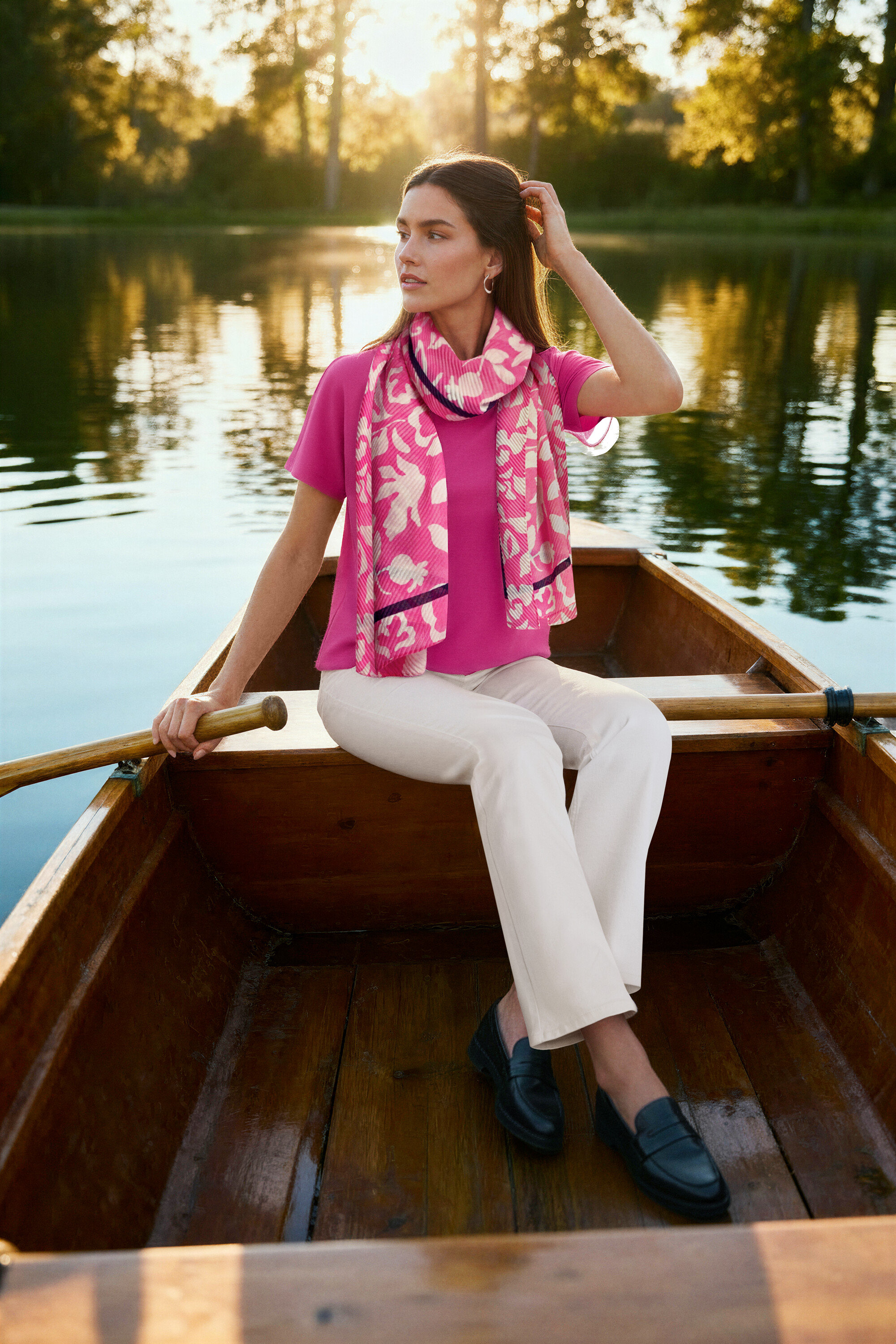 Žena sedí v lodi, má na sobě růžovou halenku, krémové bootcut džíny ‒ Fit »Lou«, kožené mokasíny a Náušnice Wave.