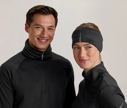 Usmívající se muž a žena v černých sportovních topech s vysokými límci a reflexními tečkami. Žena má také černou čelenku s reflexními tečkami.