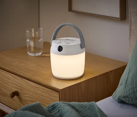 Svítící multifunkční LED svítidlo s pohybovým senzorem a šedým madlem stojí na dřevěném nočním stolku vedle sklenice vody.
