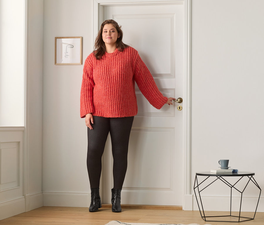 Žena stojí u dveří a má na sobě svetr z hrubé pleteniny a legíny v džínovém vzhledu s podšívkou.