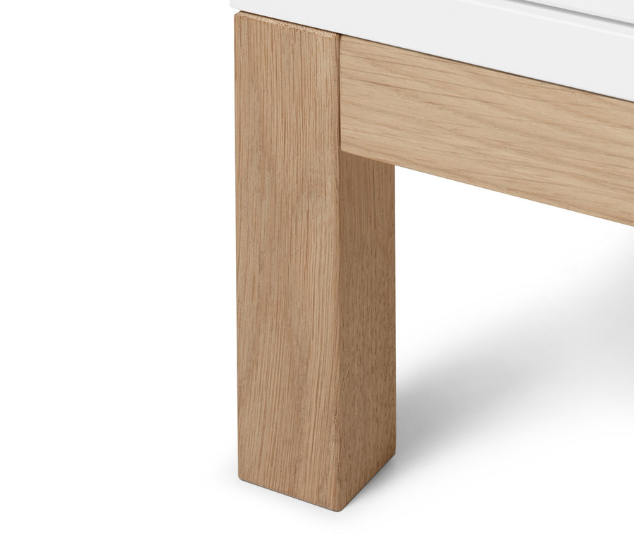 Detail spodní části vysoké skříňky »Eklund« se zásuvkami, bílá skříňka stojí na světlých dřevěných nohách.