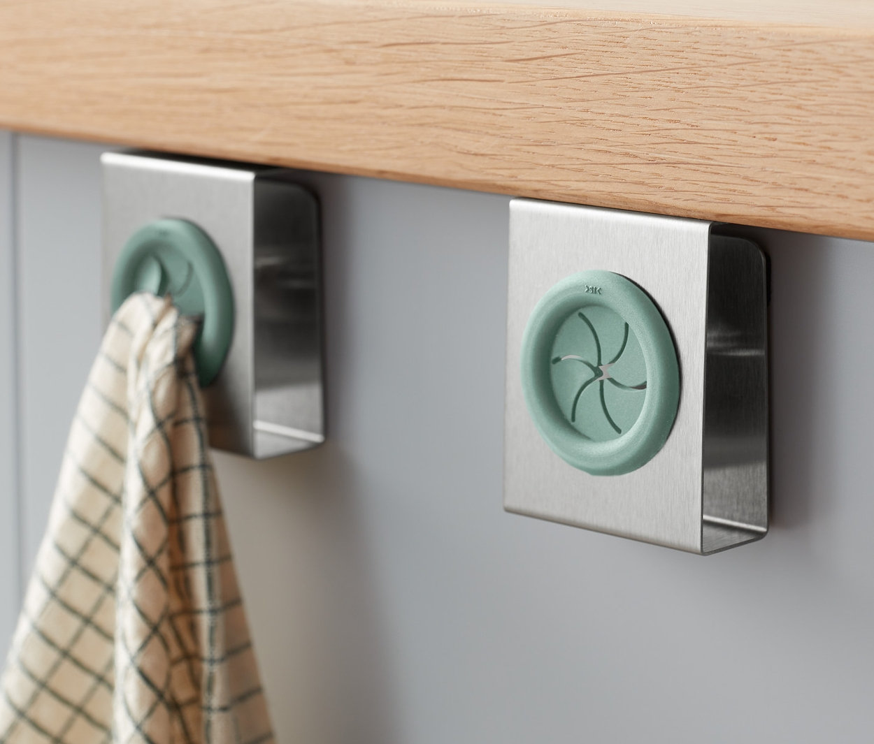 Dva držáky na kuchyňské utěrky jsou připevněny ke skříňce, na jednom z nich visí utěrka.