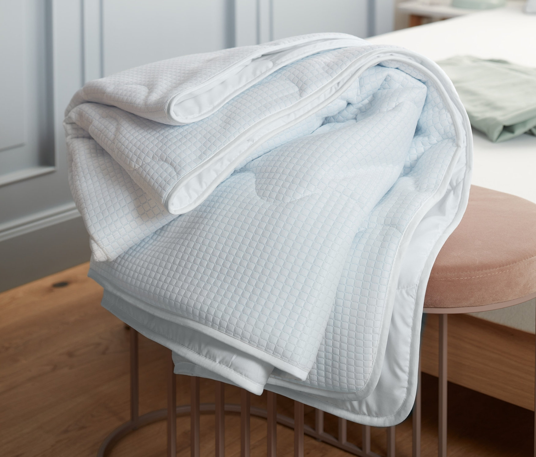 Složená chladivá přikrývka leží na růžové stoličce v ložnici.