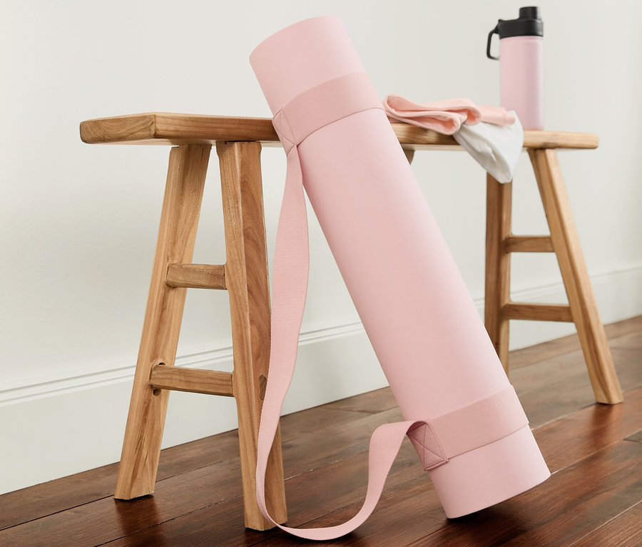 Srolovaná podložka na jógu a cvičení růžové barvy opřená o dřevěnou stoličku. Na stoličce leží složený ručník a růžová láhev na vodu.