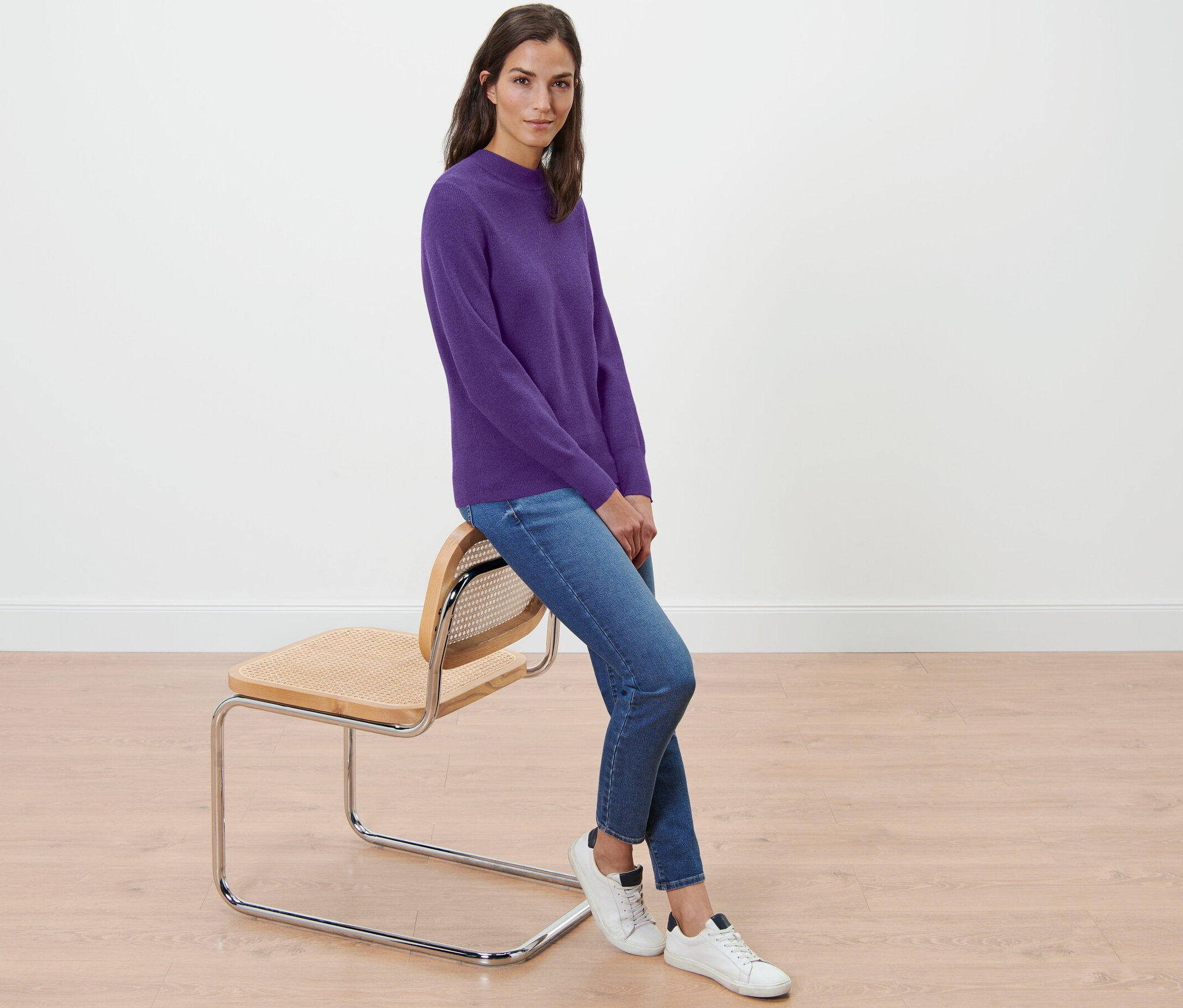 Žena sedí na židli a má na sobě fialový svetr z jemného úpletu.