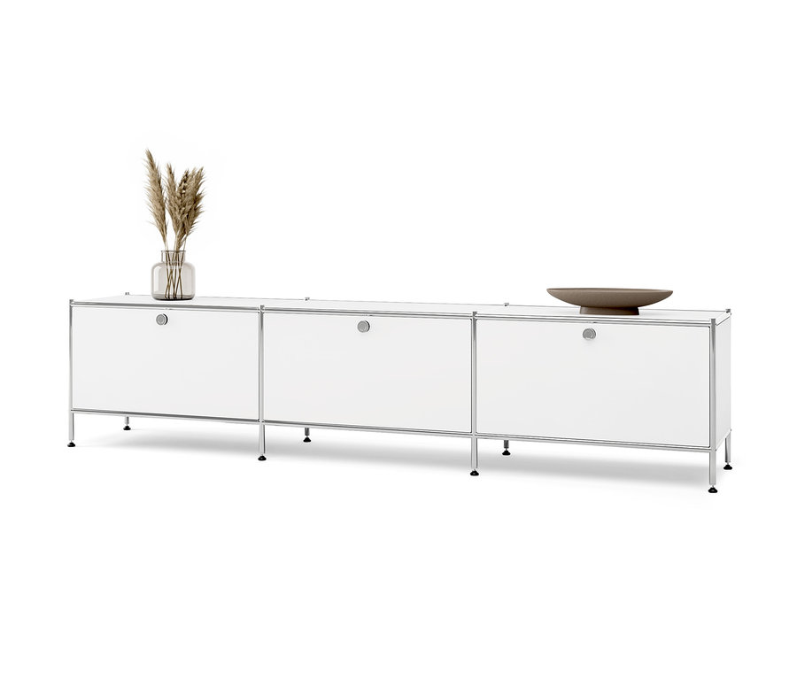 Bílá nízká kovová skříňka »CN3« se 3 výklopnými dvířky. Na skříňce váza s trávou a hnědá mísa.