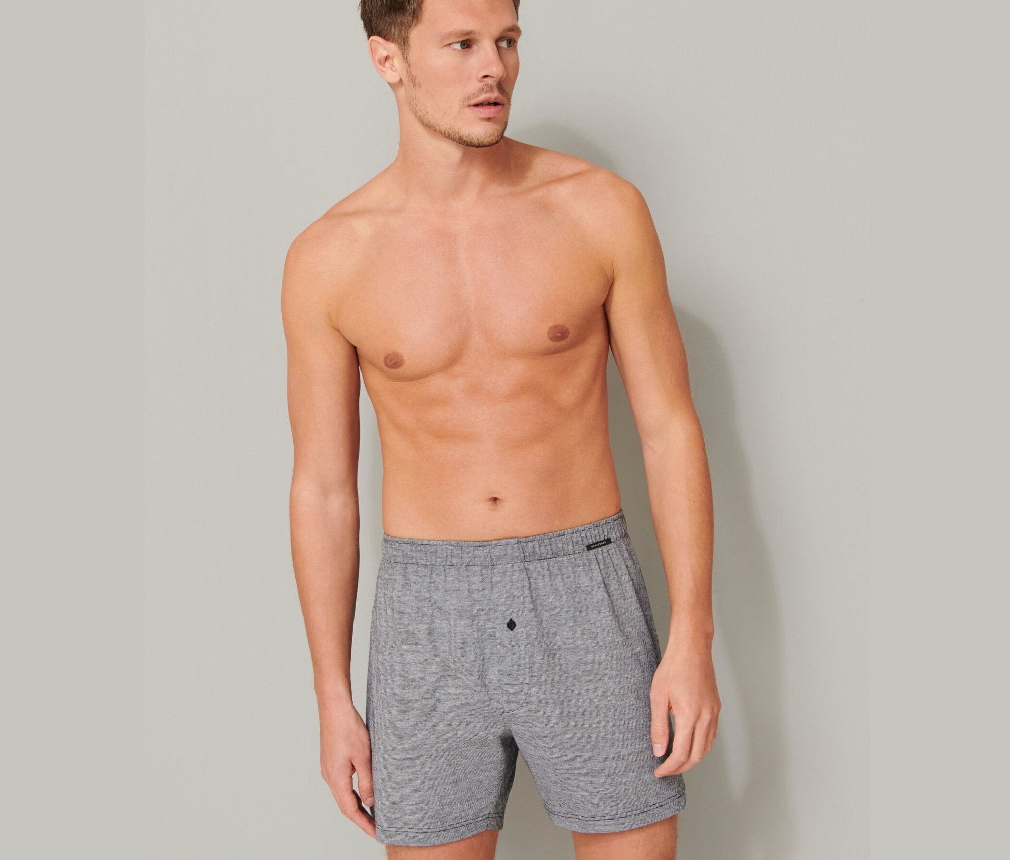 Muž s odhalenou horní částí těla pózuje ve světle šedých bavlněných boxerkách SCHIESSER, 2 ks.