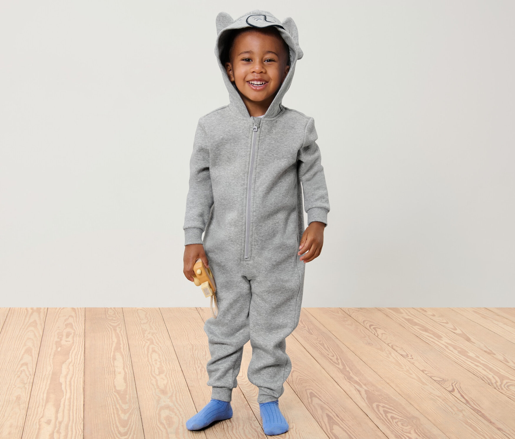 Usmívající se chlapec v šedém dětském pohodlném overalu s kapucí s ouškama.
