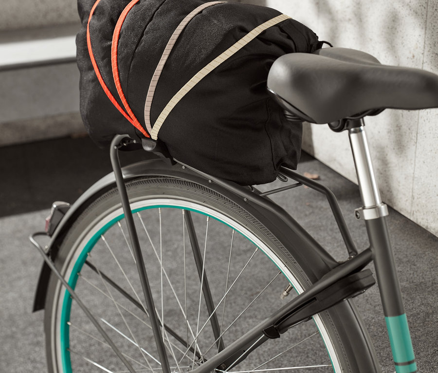 Na kole je upevněn upínací popruh na jízdní kolo, který drží černou brašnu.