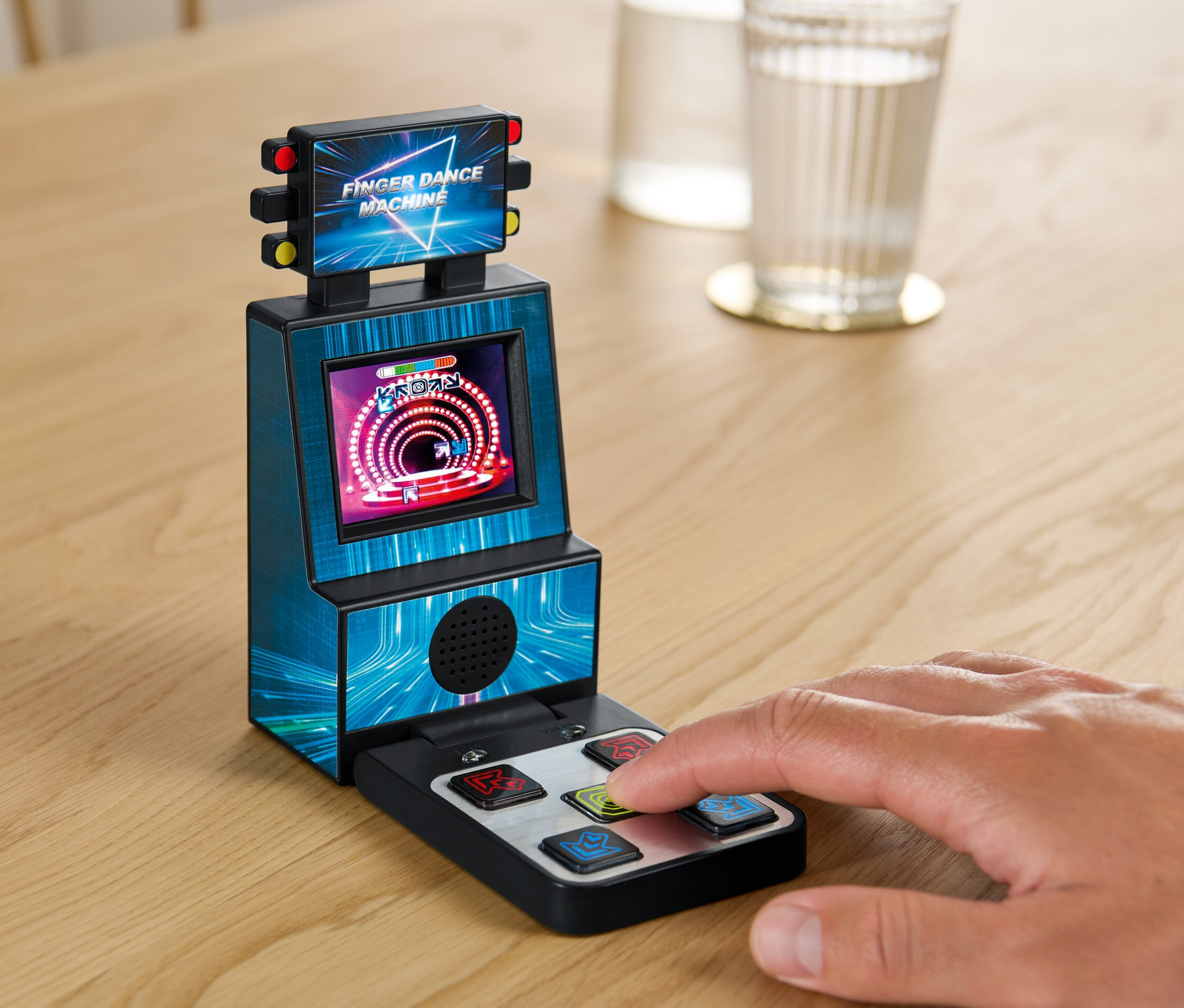 Ruka hraje na Prstovém tanečním automatu na stole vedle sklenice vody.
