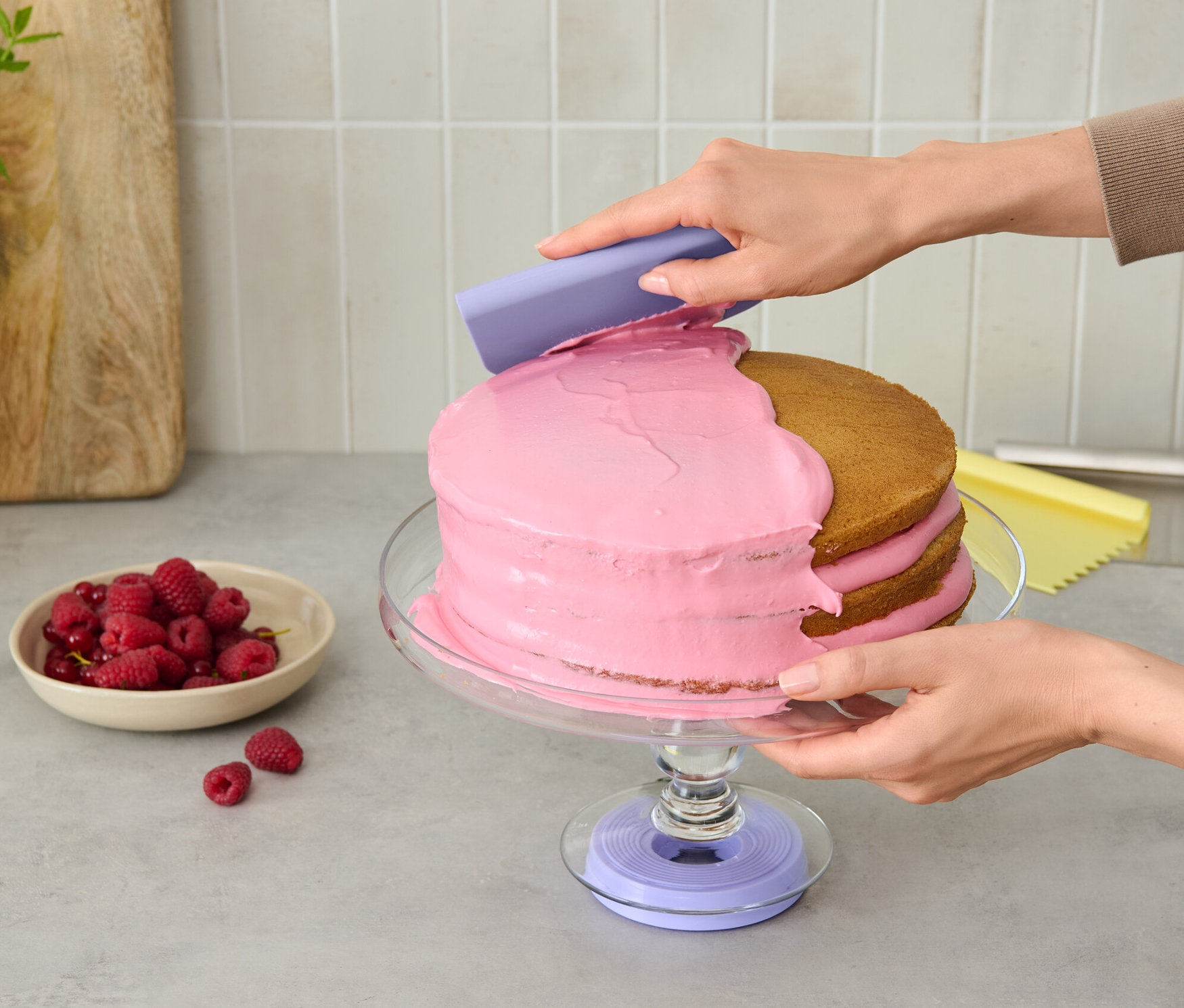 Osoba nanáší růžový krém na dort na otočné podložce na dort.