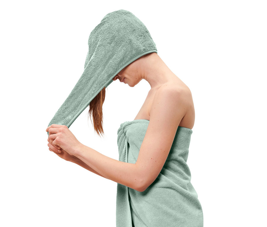 Žena si na hlavu dává světle zelený ručníkový turban a má na sobě světle zelený ručník.