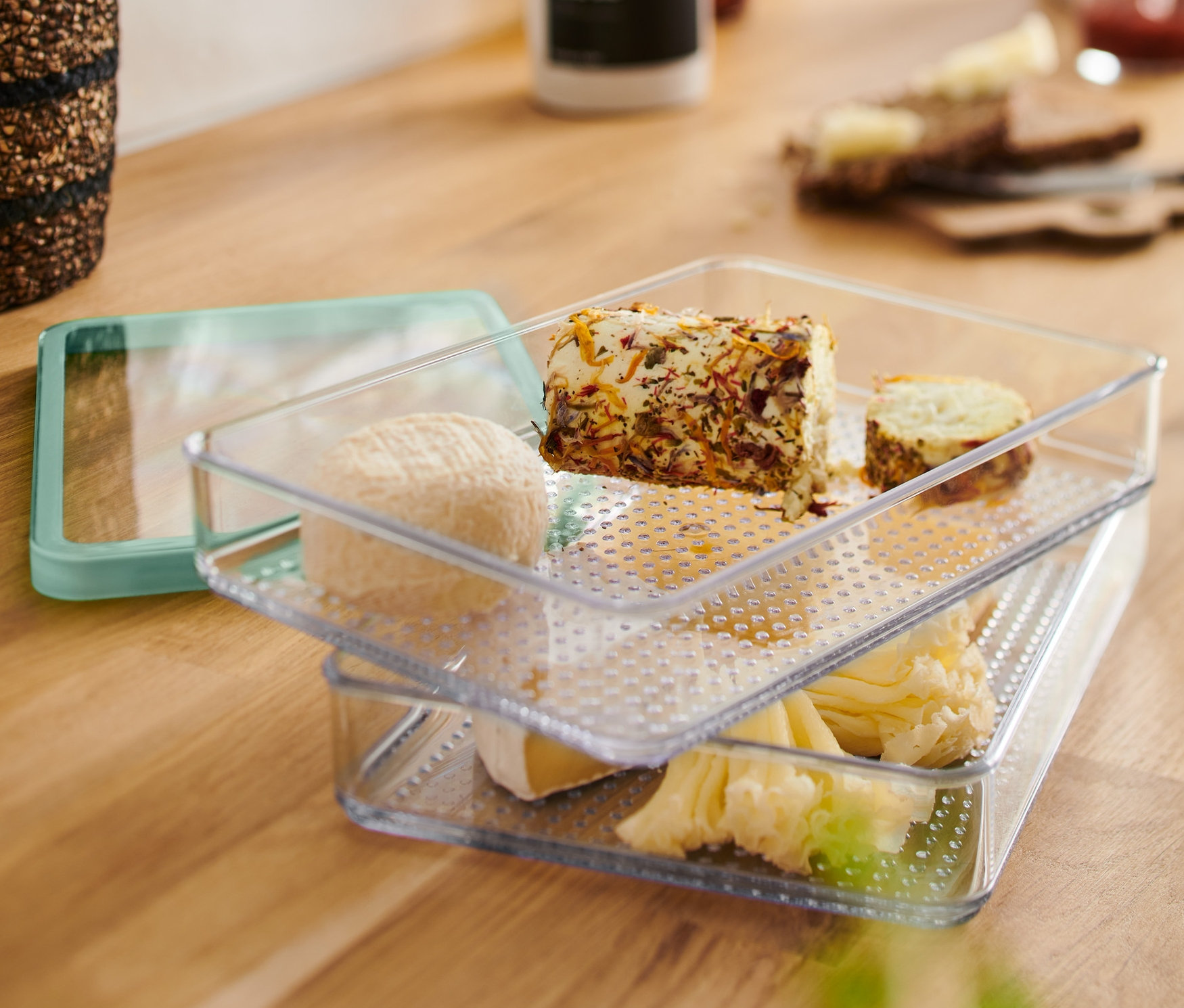 Dva průhledné Nádoby na skladování potravin v lednici naskládané na sobě s různými sýry.