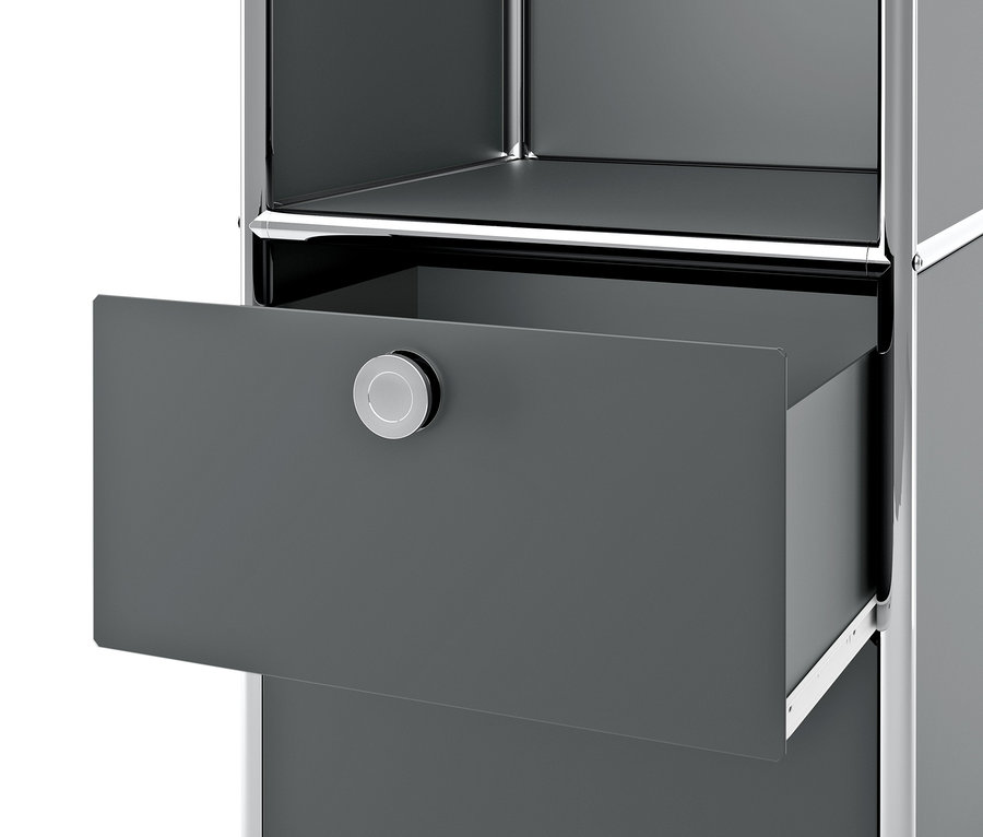 Detail šedého kovového regálu CN3 se 2 výklopnými dvířky a 2 zásuvkami, přičemž jedna zásuvka je otevřená.