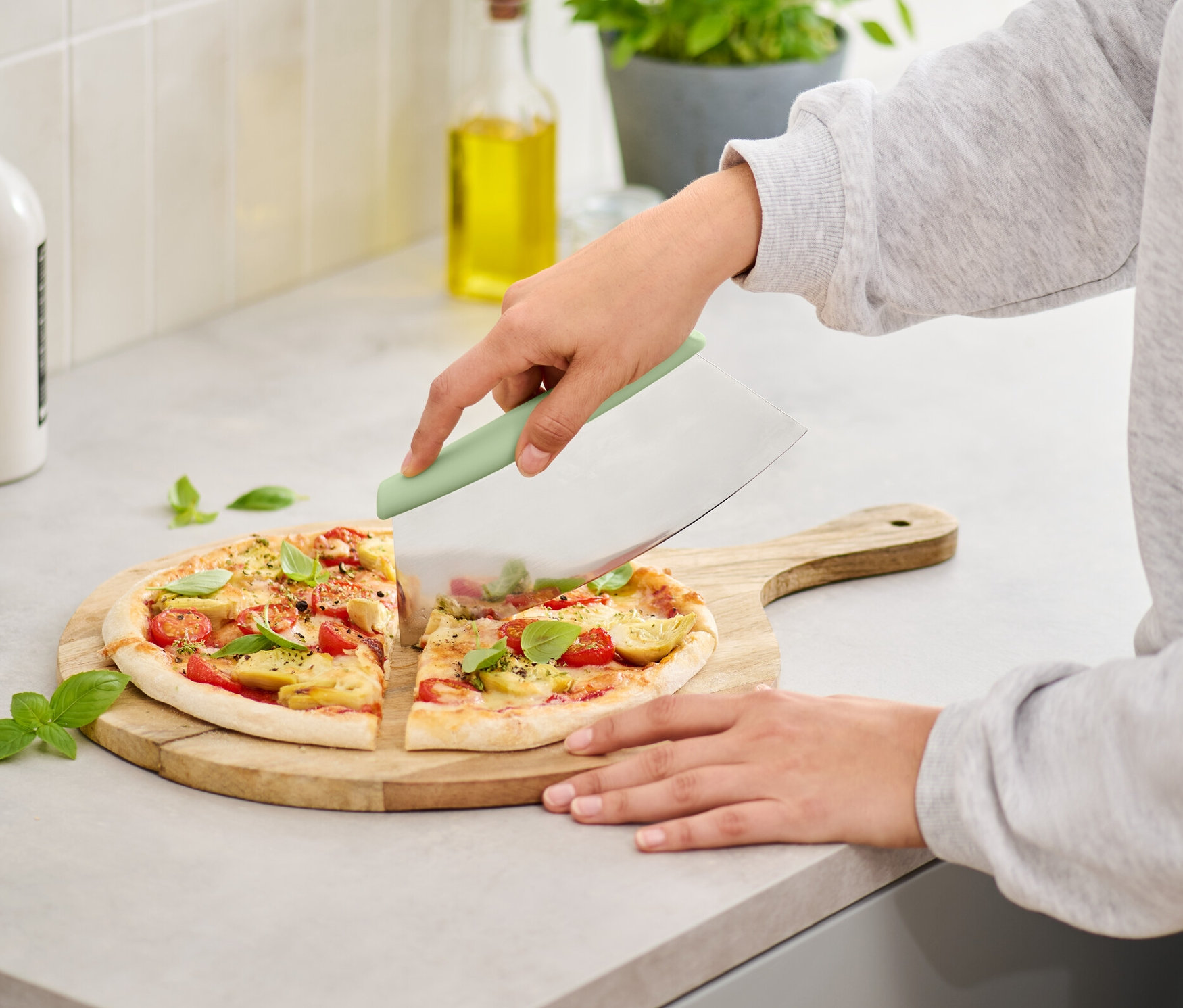 Žena krájí pizzu na dřevěném prkénku pomocí kráječe na pizzu a bylinky.