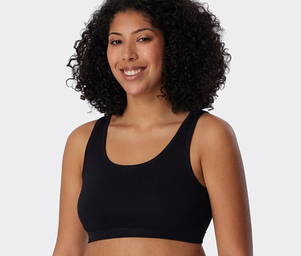 Žena s kudrnatými vlasy má na sobě černou podprsenku s biobavlnou SCHIESSER.