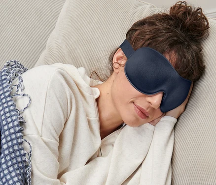 Žena spí na gauči s maskou na spaní.