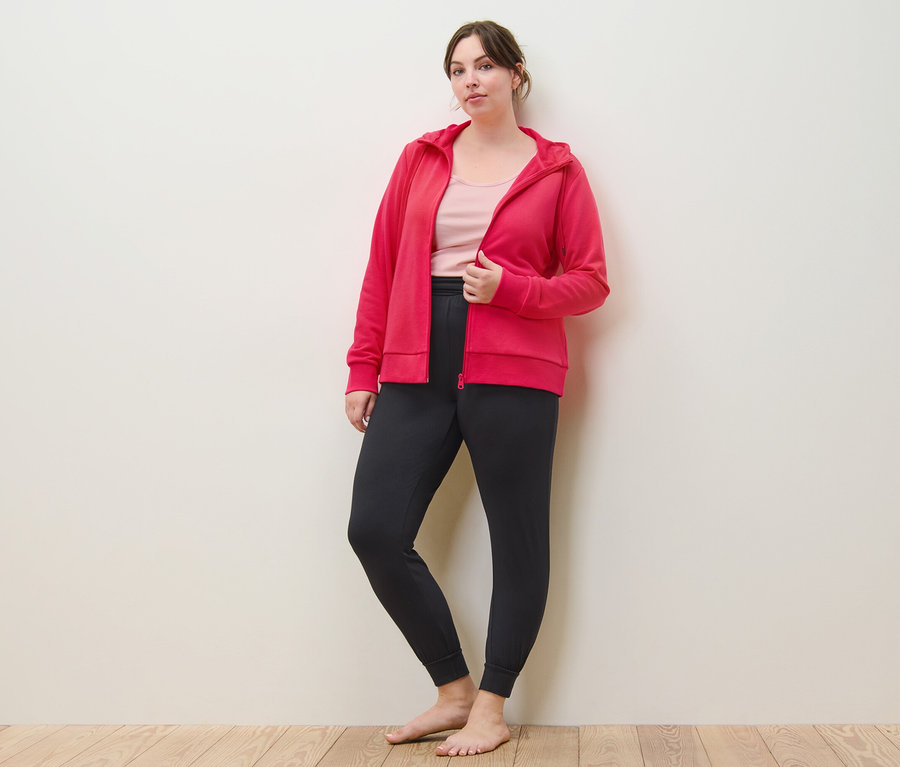 Žena pózuje v růžové mikině, topech (2 ks, světle růžová/růžová) a kalhotách na jógu.