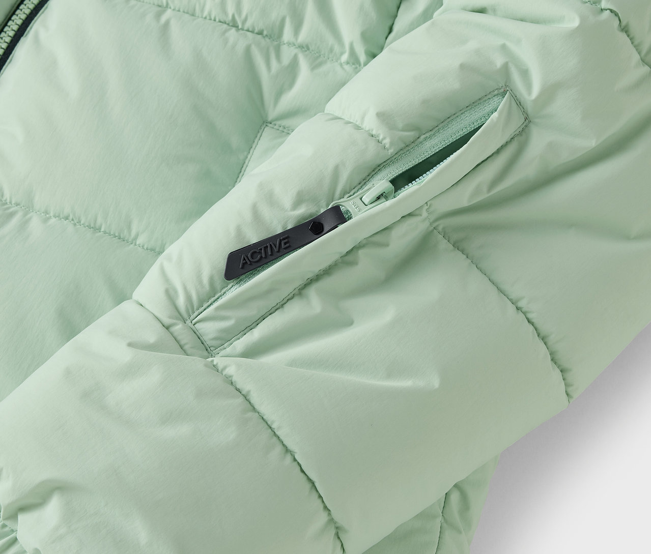 Detail světle zelené prošívané bundy s kapsou na zip.