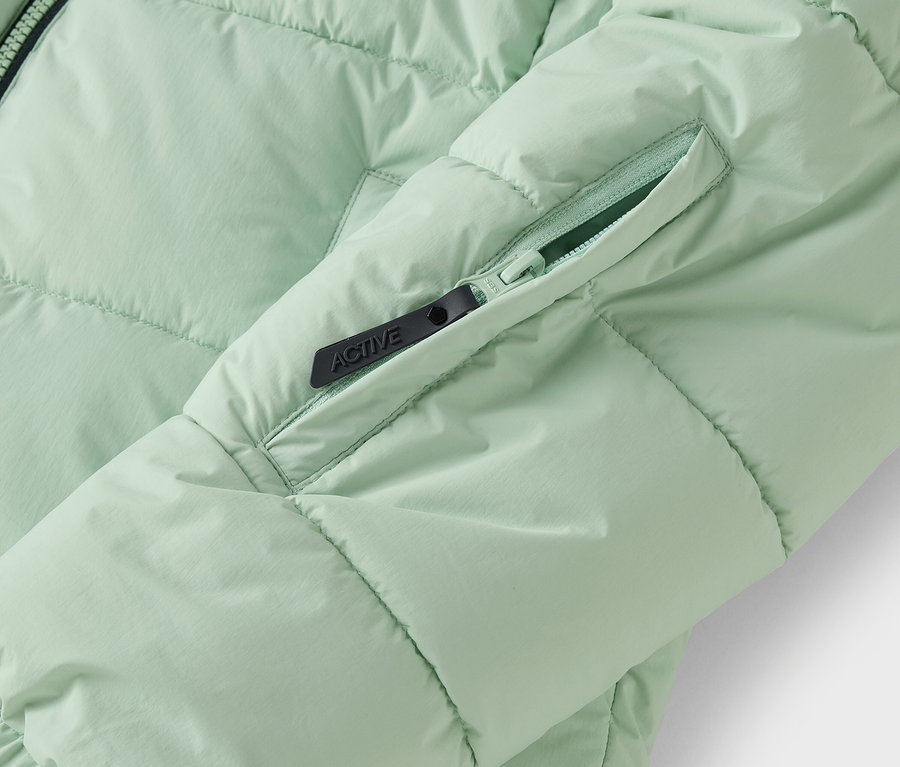 Detail světle zelené prošívané bundy s kapsou na zip.
