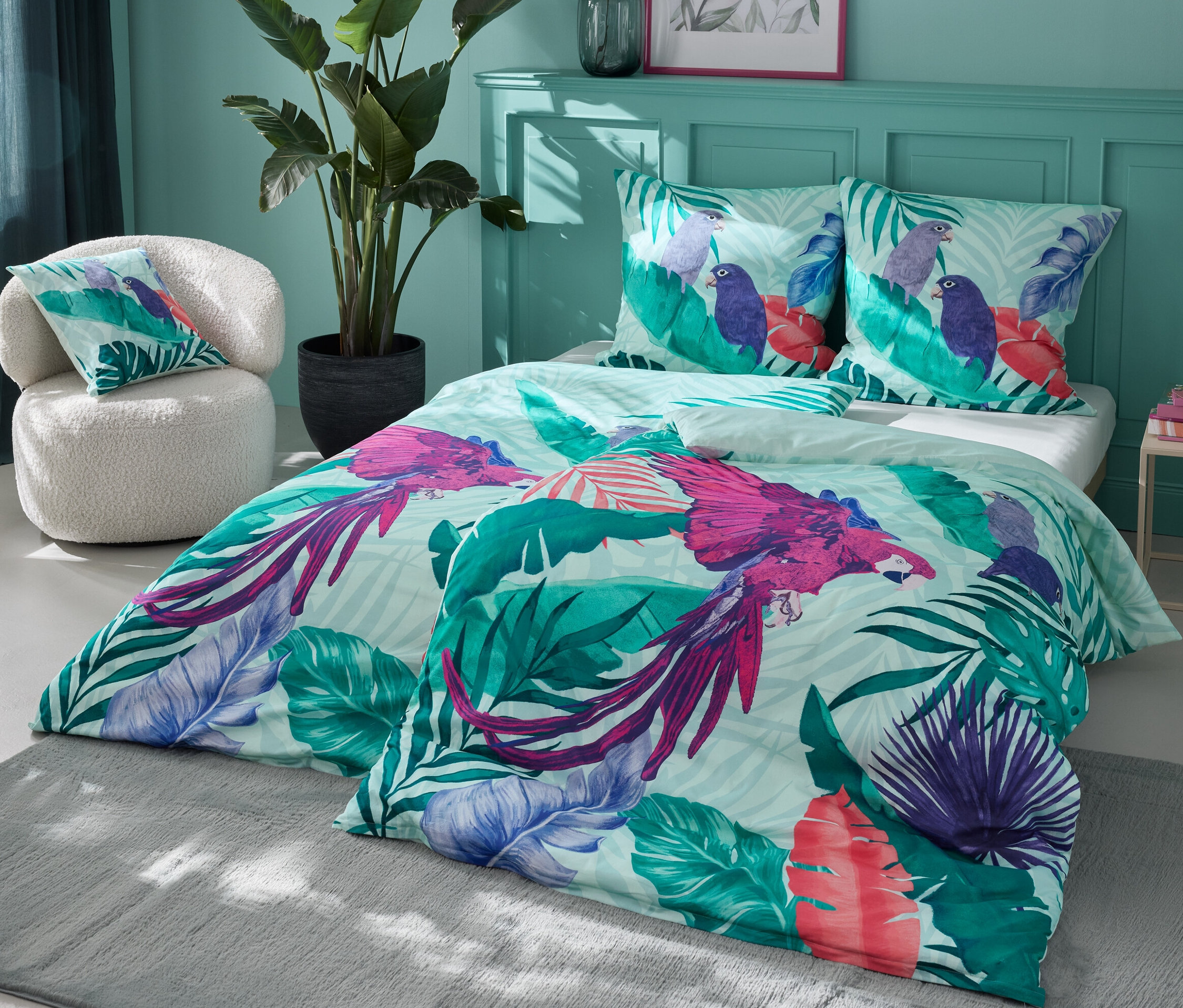 Ložní souprava s potiskem papoušků a listů. V pozadí perkálové povlečení standardní a nadměrné velikosti.