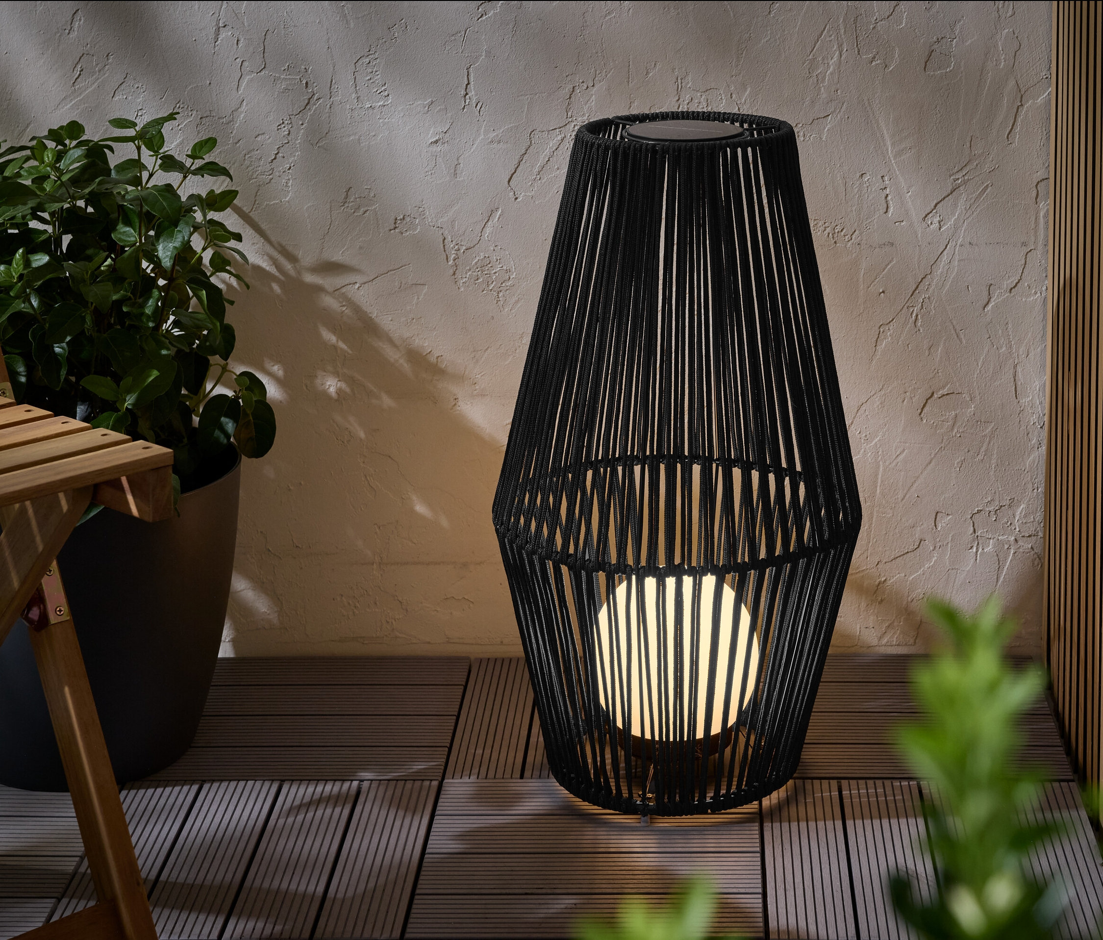 Velká solární lucerna s textilním výpletem stojí na terase.