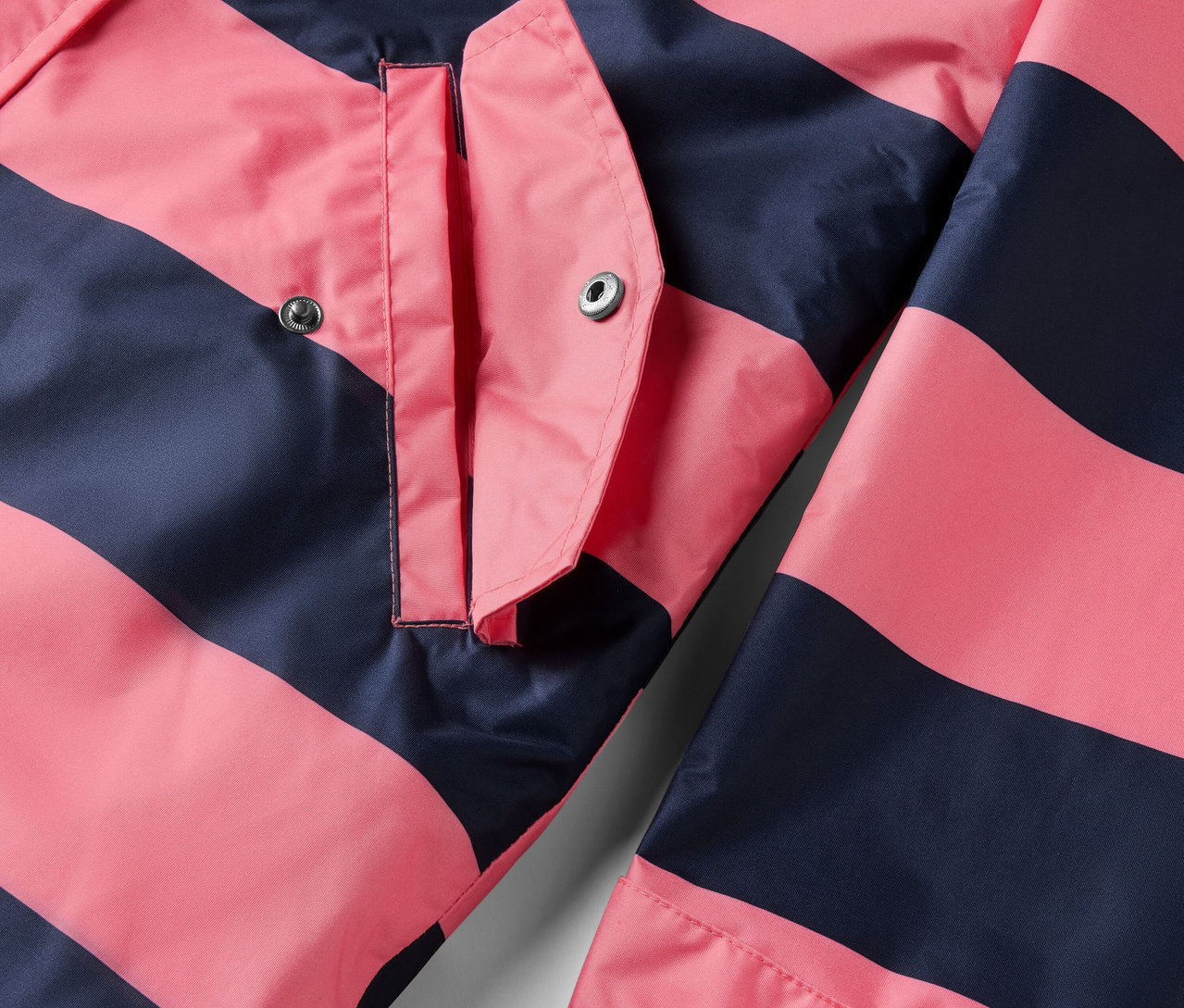 Detail bundy do deště 3 v 1 s růžovými a tmavě modrými pruhy a kapsou.