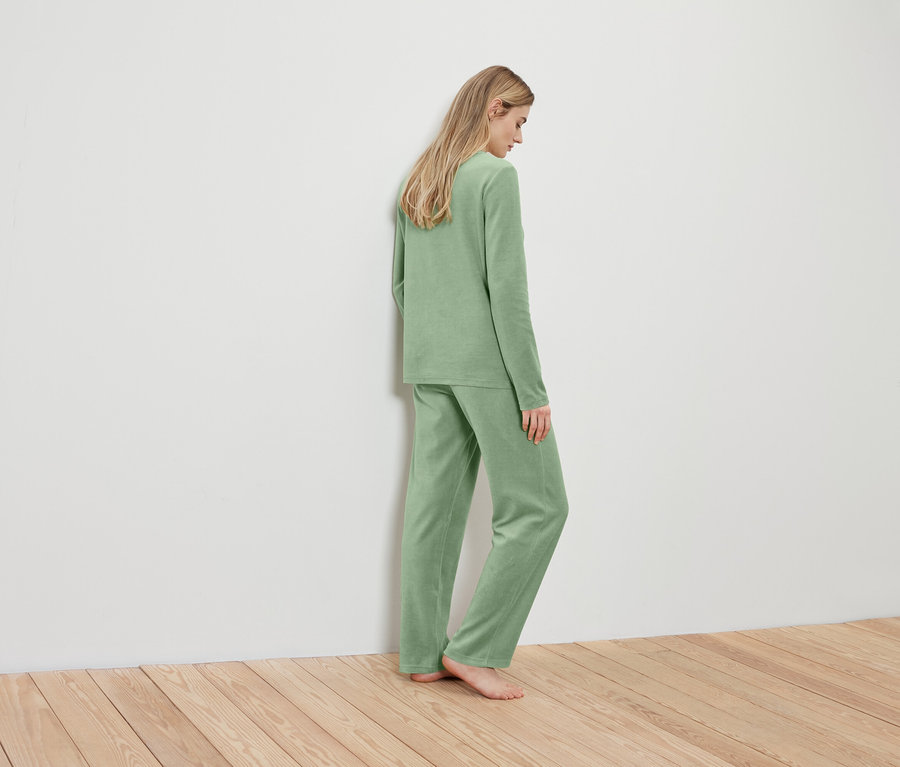 Blondýna v světle zeleném pyžamu stojí zády ke zdi.