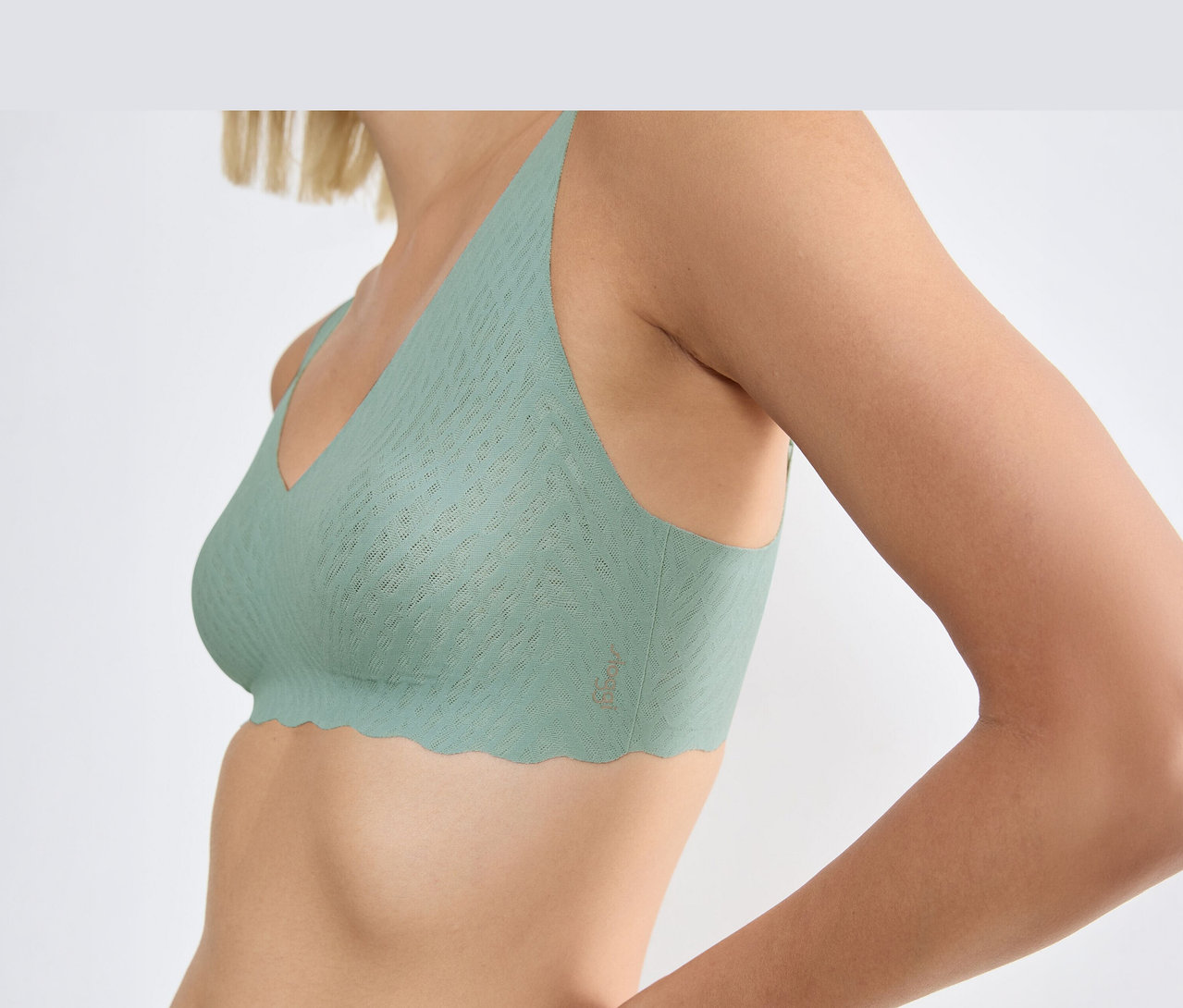Žena má na sobě měkkou podprsenku sloggi ZERO Feel Bliss Soft Bra v barvě misty turquoise s vlnitým lemem a texturovaným vzorem.