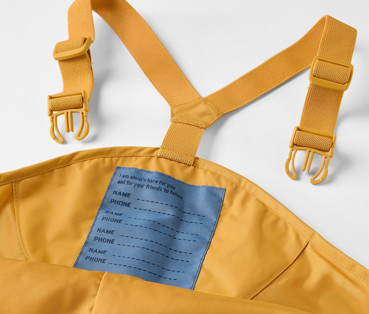 Detail dětských kalhot do deště s laclem a žlutými popruhy.