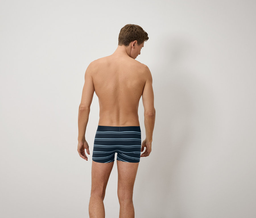Muž zády ke kameře má na sobě modré pruhované boxerky.