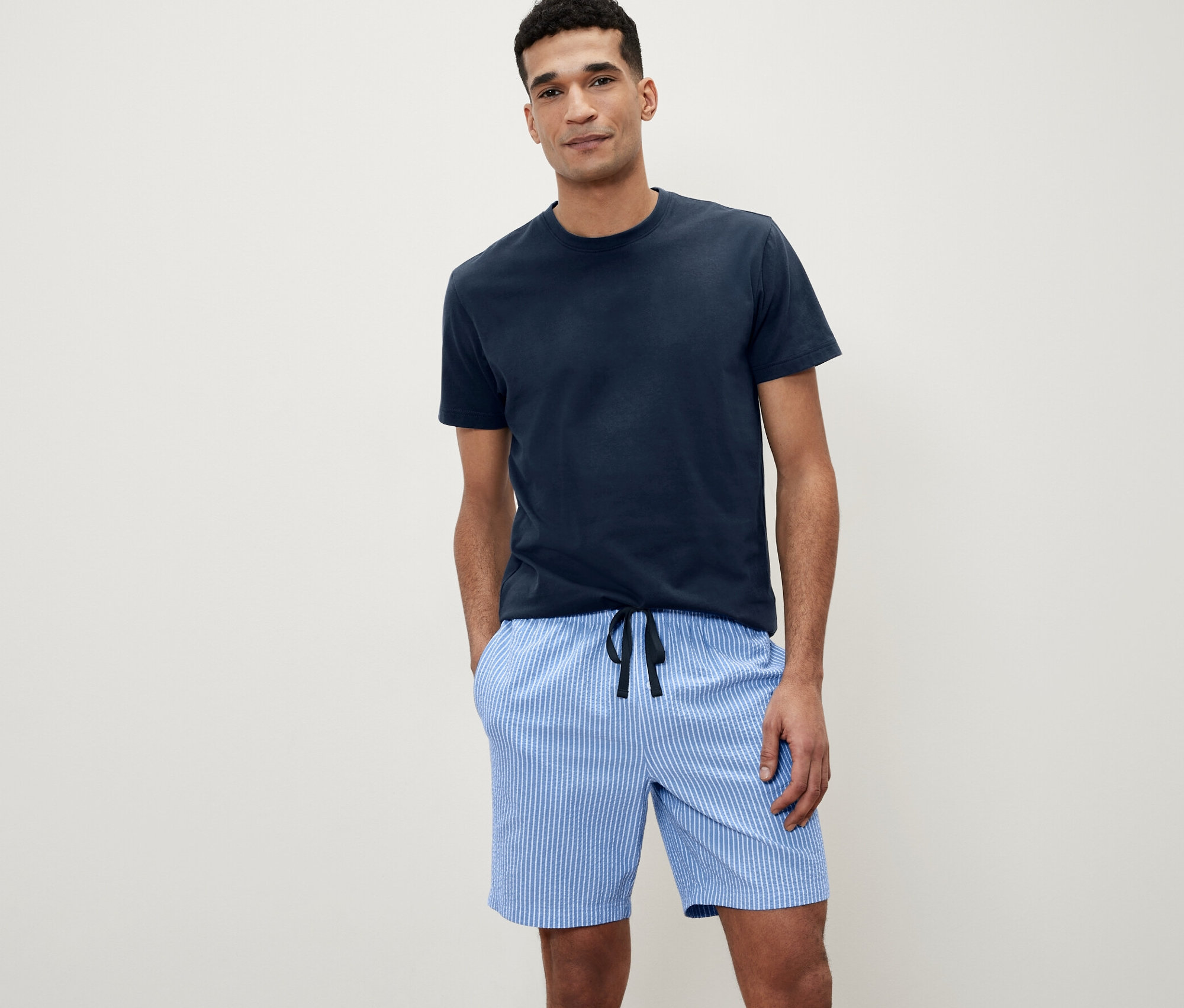 Muž pózuje v krátkém pyžamovém setu s tkanými kalhotami.