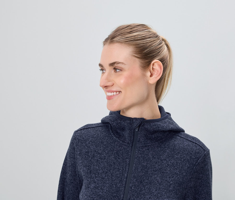 Profil usmívající se ženy s blond vlasy v modré mikině s kapucí na zip.