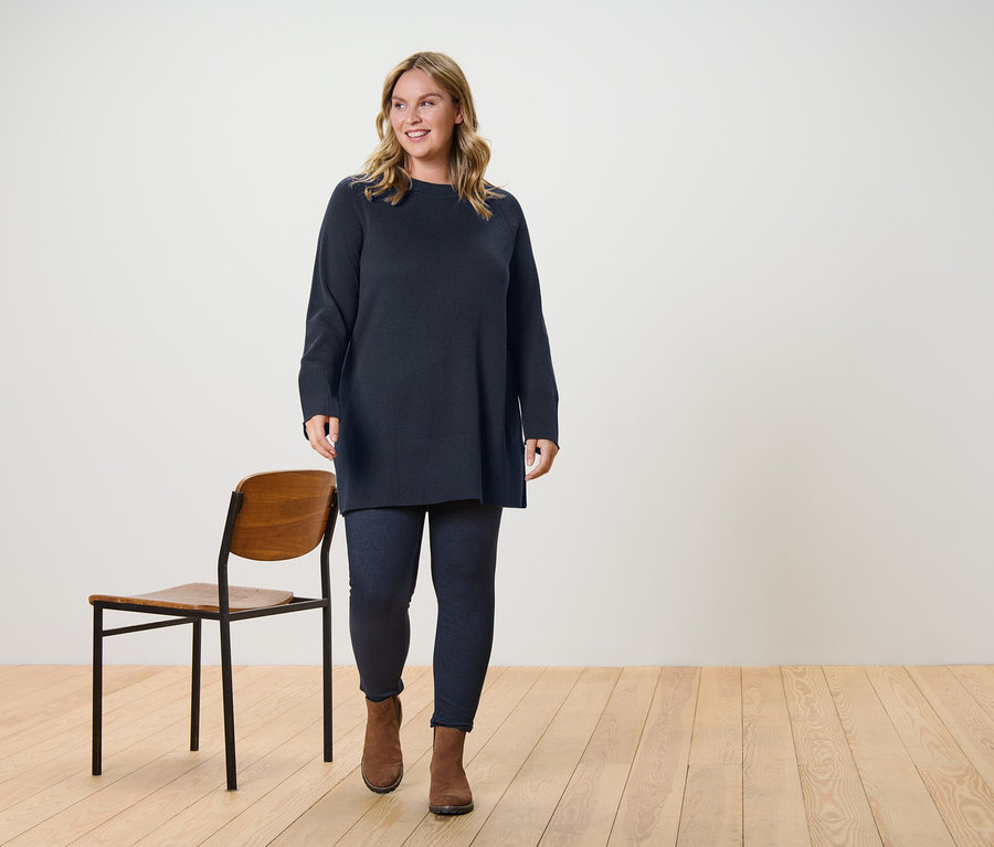 Žena kráčí a má na sobě dlouhý pletený svetr tmavě hnědé barvy a legíny v džínovém vzhledu s podšívkou.