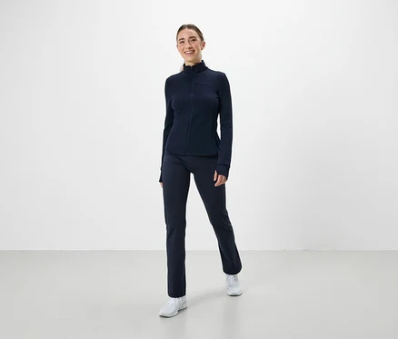Žena má na sobě tmavě modrý sportovní set a bílé tenisky.