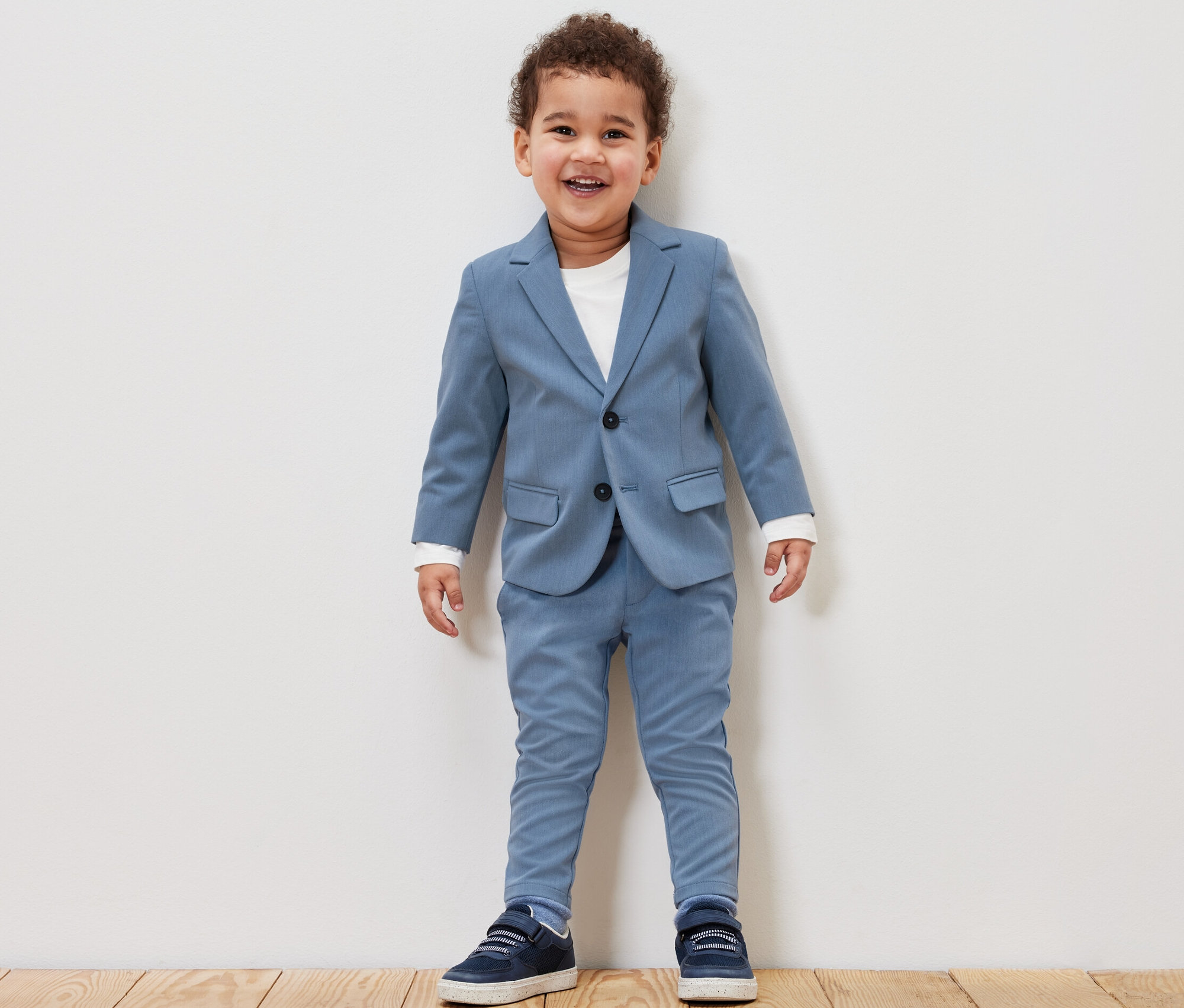 Usmívající se chlapeček v dětském saku a kalhotách chino modré barvy.