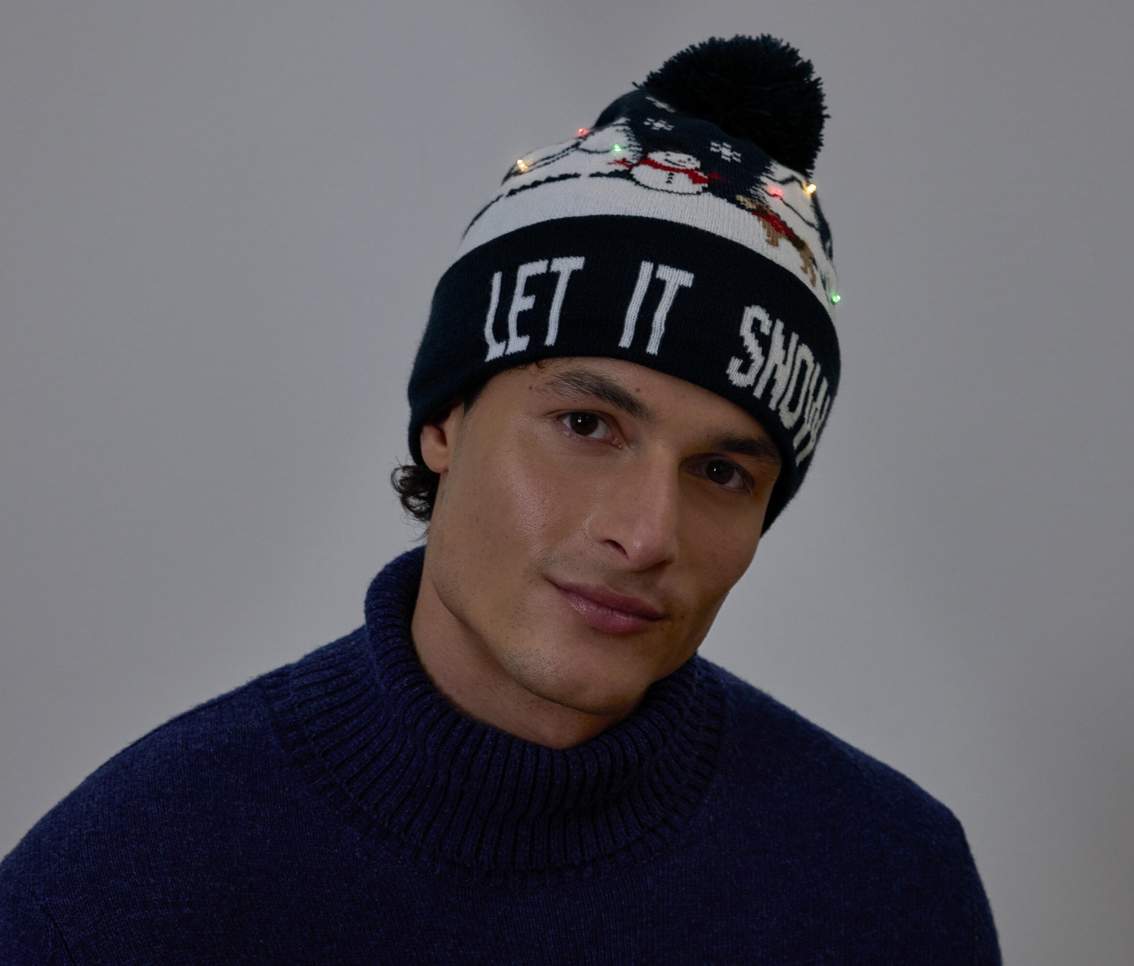 Portrét muže s vánoční čepicí s nápisem LET IT SNOW a malými světýlky.
