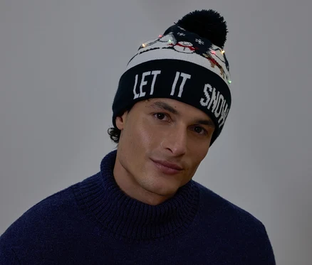 Portrét muže s vánoční čepicí s nápisem LET IT SNOW a malými světýlky.