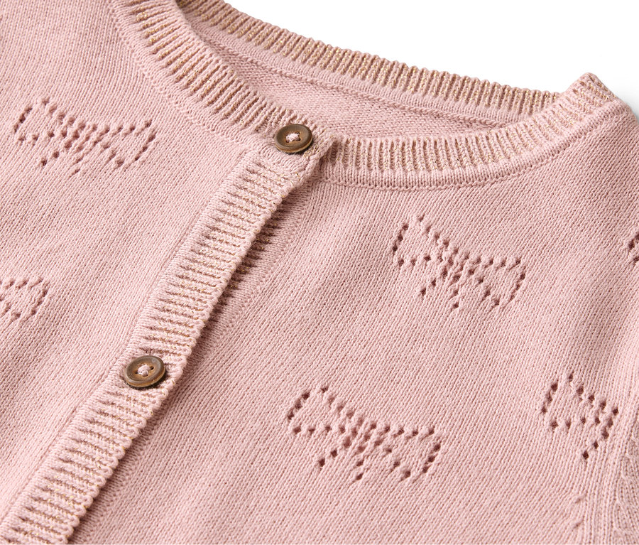 Detail růžového svetru s knoflíky a vzorem mašlí.