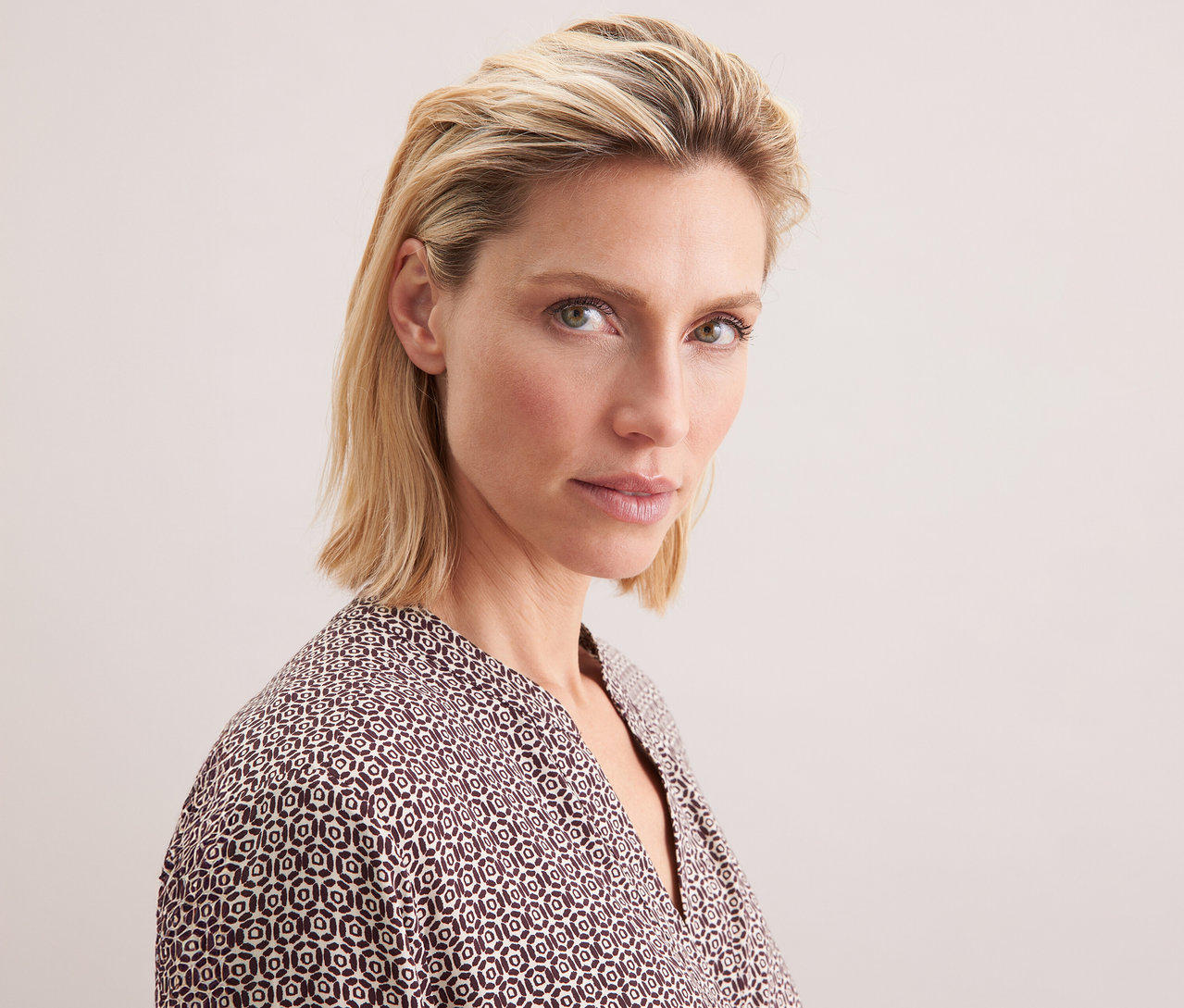 Portrét blondýny v tunice z viskózy Seidensticker s celoplošným potiskem v ecru a burgundské barvě.