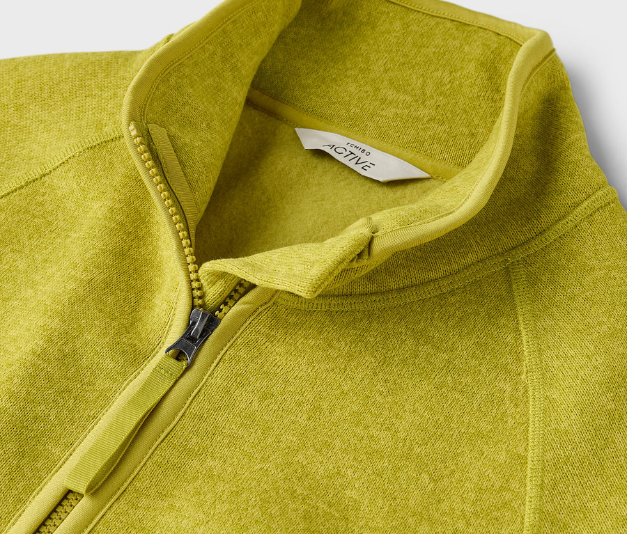 Detailní záběr na žlutozelenou mikinu s aktivním zipem.