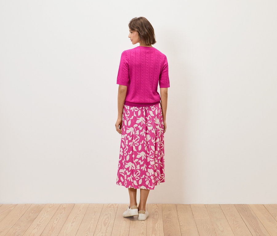 Žena stojí zády, má na sobě růžový top a sukni s květinovým vzorem.