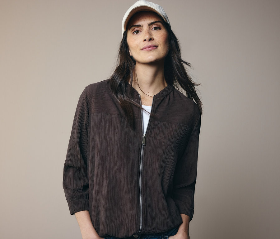 Žena v hnědé bundě a bílé kšiltovce.