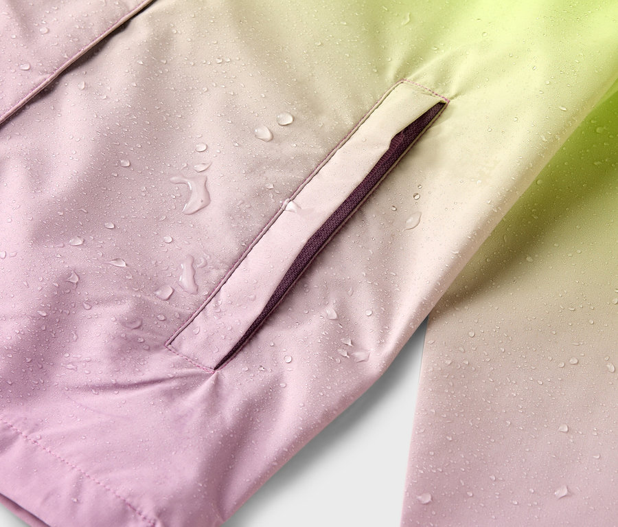 Detailní záběr na voděodolnou bundu s barevným gradientem od růžové po žlutou s kapkami deště a boční kapsou.