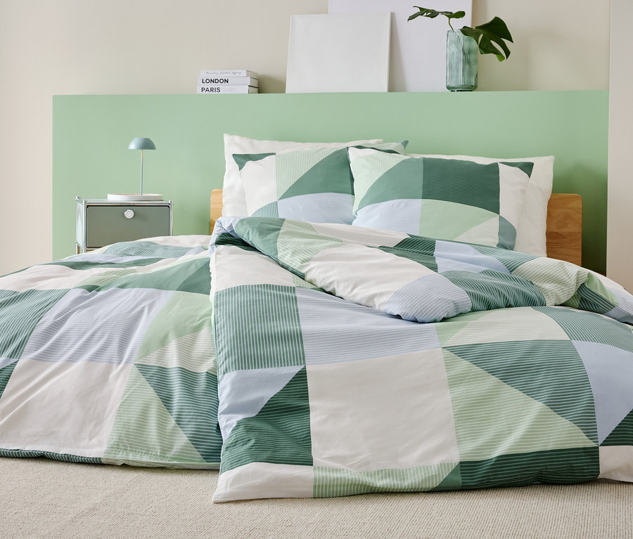 Postel se zeleno-bílo-modrou patchworkovou přikrývkou a odpovídajícími povlaky na polštáře stojí v ložnici.
