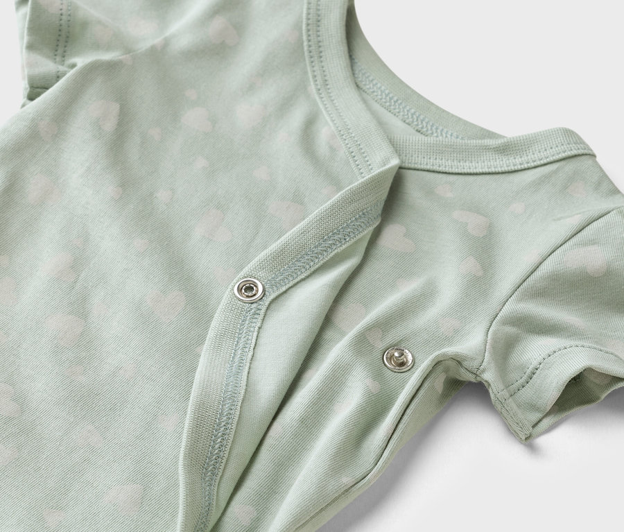 Detailní záběr světle zeleného dětského body s bílým vzorem srdíček a patentkami.