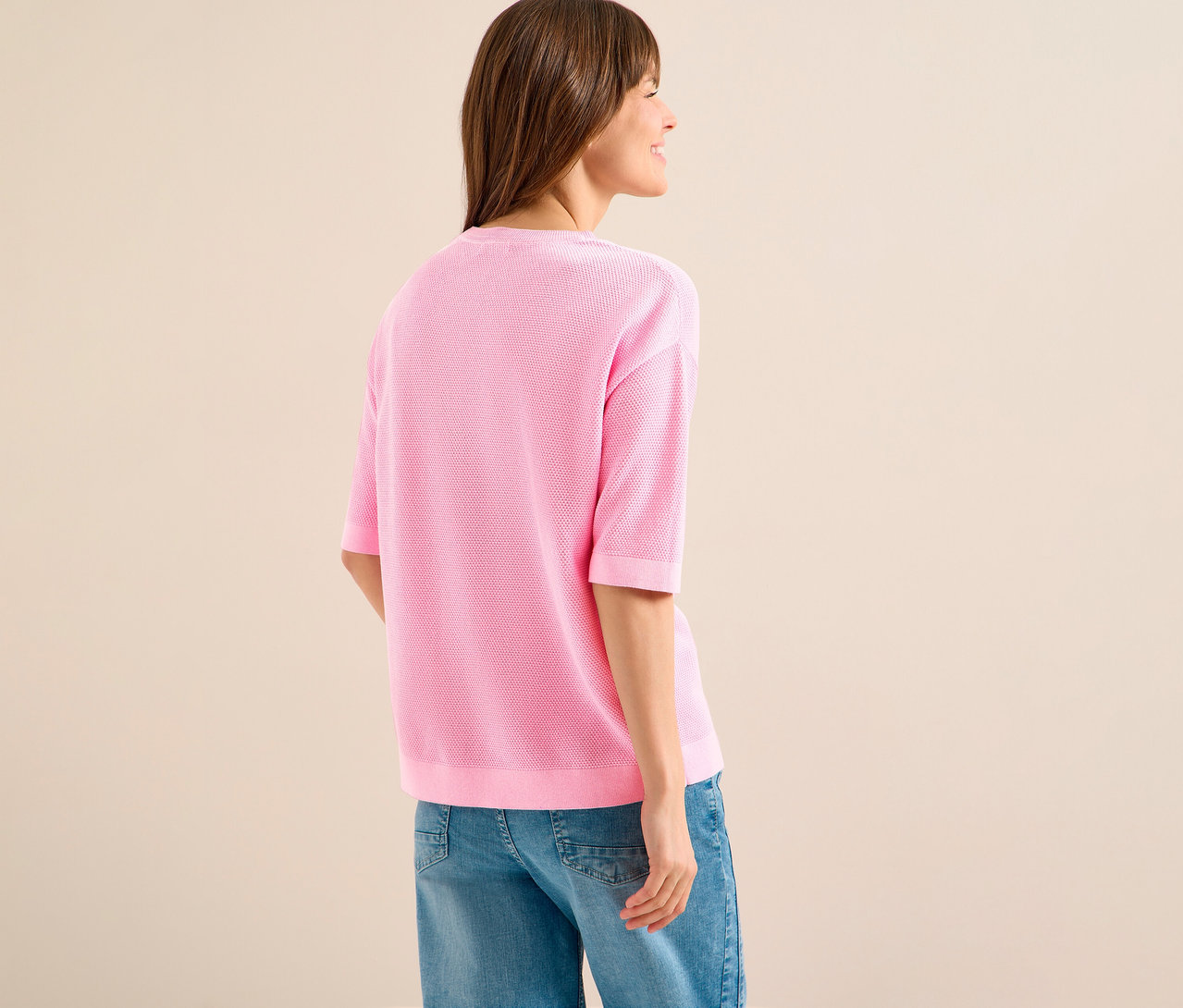 Žena zezadu v růžovém svetru s krátkým rukávem CECIL a džínách.