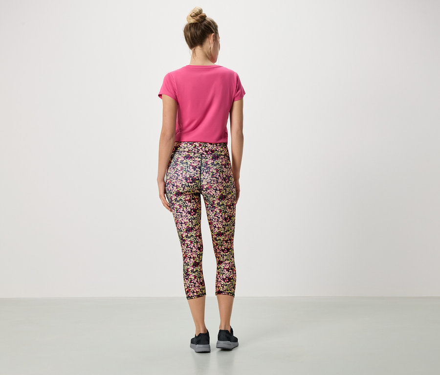 Pohled zezadu na ženu s drdolem, která má na sobě růžové tričko a květinové legíny.