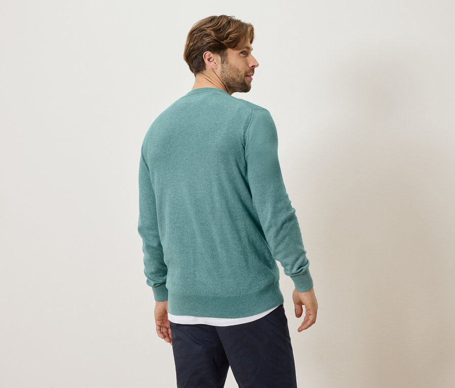 Muž zezadu v tyrkysovém svetru a modrých kalhotách.