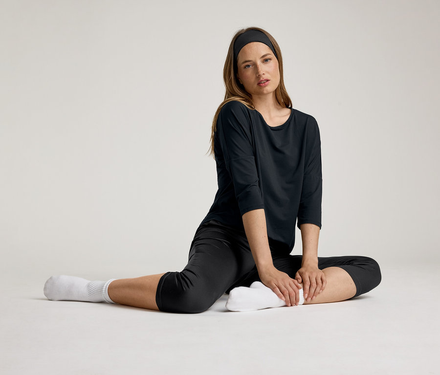Žena sedí v černém 3/4 sportovním tričku. Má čelenku a bílé ponožky.